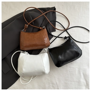 Three minimalist semi-circle crossbody bags in black, white, and brown with thin knotted straps