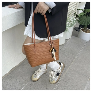 Detailed close-up of brown woven tote bag featuring a leather weave and beaded charm pendant