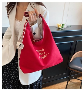 Detail of red canvas tote bag with letter embroidery and leather handle on a model