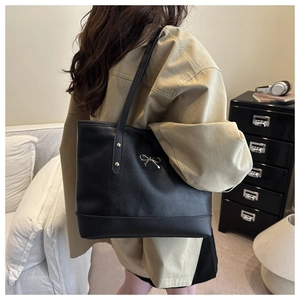 Detail of black tote bag with gold metal bow charm and reinforced rivet shoulder straps