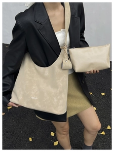 Close-up of beige matte leather hobo bag and pouch set on a fashion model in the city