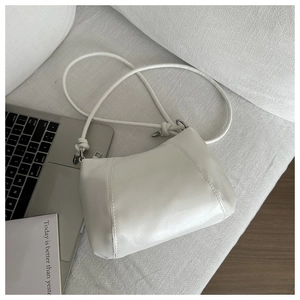Minimalist white leather hobo bag with unique knotted strap detail on a sofa