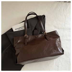 Close-up of dark brown tote bag showing supple leather texture and gold metal buckle