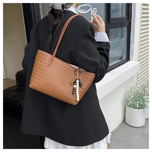 Detail der gewebten braunen Ledertasche mit buntem Perlenanhänger und schmalem Gurt