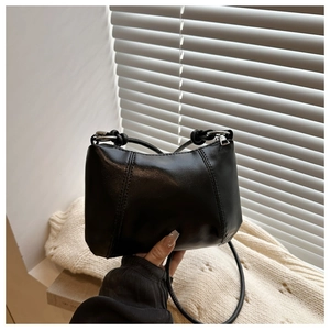 Detail of black faux leather shoulder bag with decorative stitching and silver metal buckle