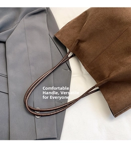 Detail of a brown suede tote bag handle with high-quality stitching and smooth texture