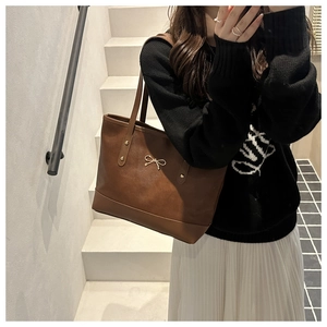 Detail of vintage brown tote bag with gold bow ornament on elegant female model