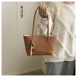 Détail d'un sac fourre-tout tressé marron avec pompon en perles et fines anses en cuir