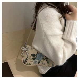 Detail of beige jacquard saddle bag with vintage floral embroidery and silver bead charm
