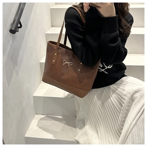 Detail of a brown tote bag featuring golden bow buckle and rivets on soft leather
