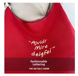 Detailed close-up of white letter embroidery on a red canvas tote bag showing stitching