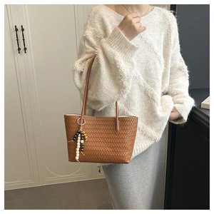 Detail of brown woven tote bag with wooden bead tassel and slender shoulder strap