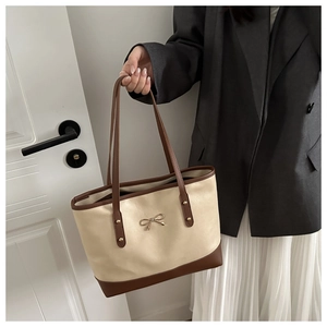 Detail of cream tote bag featuring brown leather straps and gold bow metal hardware