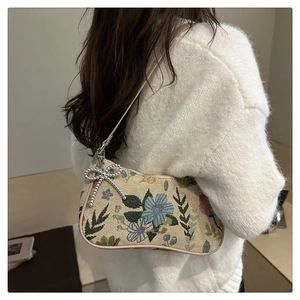 Close-up of vintage floral embroidery and beaded bow charm on canvas underarm bag