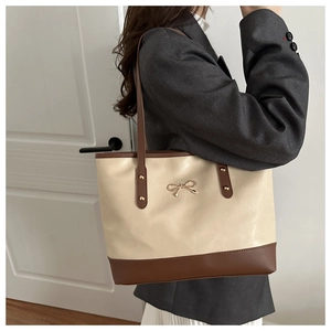 Detail of cream and brown tote bag with metal bow logo shown on shoulder