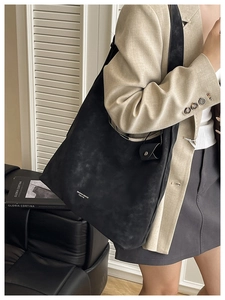 Detail of a large black matte leather hobo bag with adjustable strap and white logo