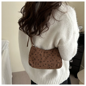 Detail of a brown corduroy underarm bag with black heart patterns on a white sweater