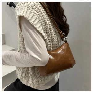 Close-up of brown glossy shoulder bag with knot detail and metallic rings on the strap