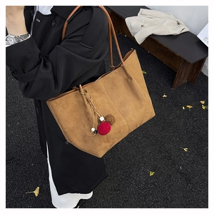 Detail of vintage brown suede tote bag with decorative plush ball and wooden bead charm