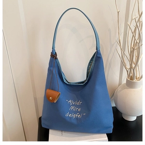 Detail of navy blue canvas tote bag with white embroidery and brown leather charm