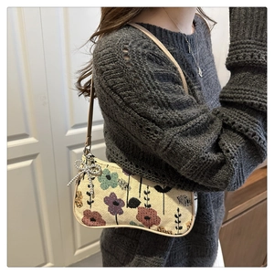 Floral patterned canvas underarm bag with a decorative silver bow pendant on model