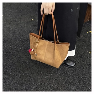 Close-up of brown suede tote bag with stylish pompom detail on ginkgo leaf background