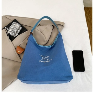 Detailed view of blue canvas tote bag with white cursive embroidery for casual style