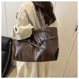 Detail of dark brown leather tote bag with metallic buckle shown on model shoulder
