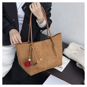 Detail of a large brown suede tote bag featuring a tassel and faux fur ball charm