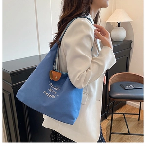 Detail view of blue canvas tote bag featuring white letter embroidery and leather buckle