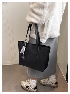 Close-up of black leather tote bag featuring contrast stitching and a printed silk scarf detail
