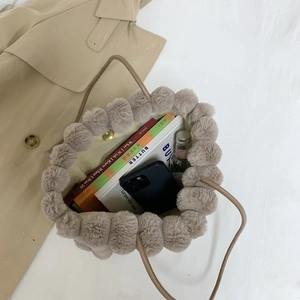 Fuzzy beige tote bag with pom-pom trim and leather handles on a trench coat background