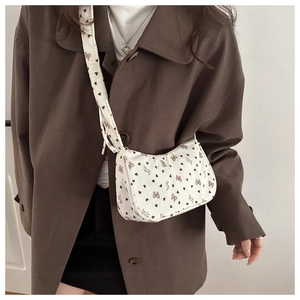 Detail of a beige corduroy half-moon crossbody bag with brown heart and bow patterns