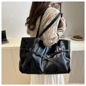 Detail of a black large-capacity tote bag with glossy leather and gold ring hardware