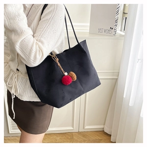 Detail of black suede tote bag with decorative red and brown fur pom-pom charms
