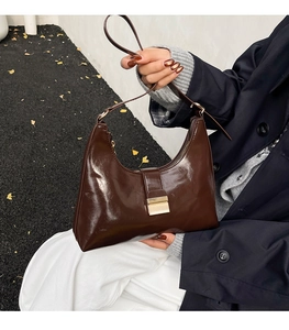 Close-up of retro dark brown glossy leather crescent bag with golden square metal buckle