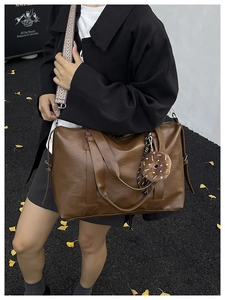 Brown leather tote bag with patterned strap and donut charm on an autumn background