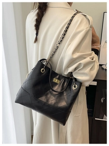 Close-up of black quilted bucket bag with gold chain strap and turn-lock closure on model