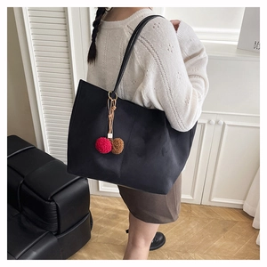 Close-up of a large black matte tote bag featuring a decorative plush ball pendant