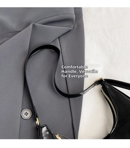 Detail of adjustable shoulder strap and gold-tone zipper on glossy black underarm bag