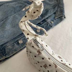 Beige corduroy crescent bag with heart bow print and silver zipper over denim background