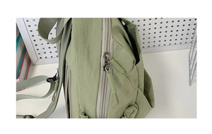 Detail view of the light green nylon backpack featuring dual zippers with long pull tabs
