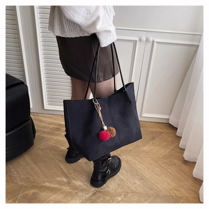 Detail of large black suede tote bag with decorative dual-color fur pompom charms