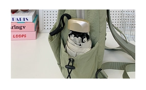 Detail of green backpack side pocket with drawstring holding an ivory folding umbrella