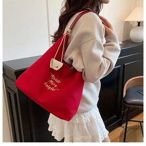 Detail of red canvas tote bag featuring white artistic lettering and leather charm