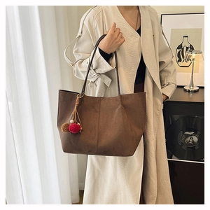 Detail of a large brown suede tote bag with stylish plush pom-pom charms and slim straps