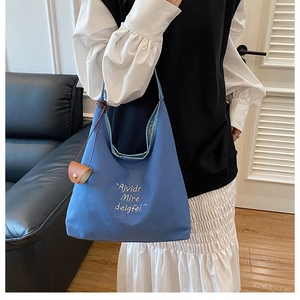 Detail of blue canvas tote bag featuring white embroidery and a brown leather pendant charm