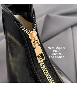 Detailed close-up of golden metal zipper pull on a glossy black leather shoulder bag