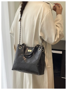 Detail of black quilted shoulder bag with gold turn-lock closure and chain strap