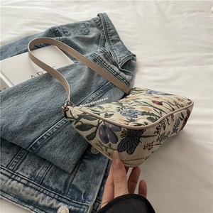 Floral canvas underarm bag with blue flower pattern and pearl chain strap on bed